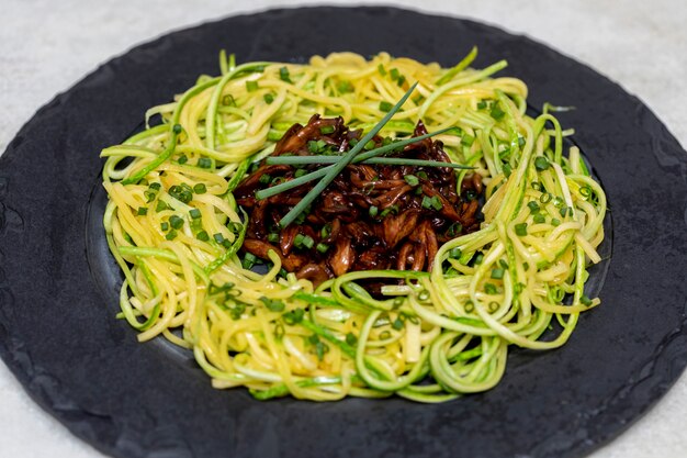 Foto courgettespaghetti met shimeji op zwarte stenen plaat.