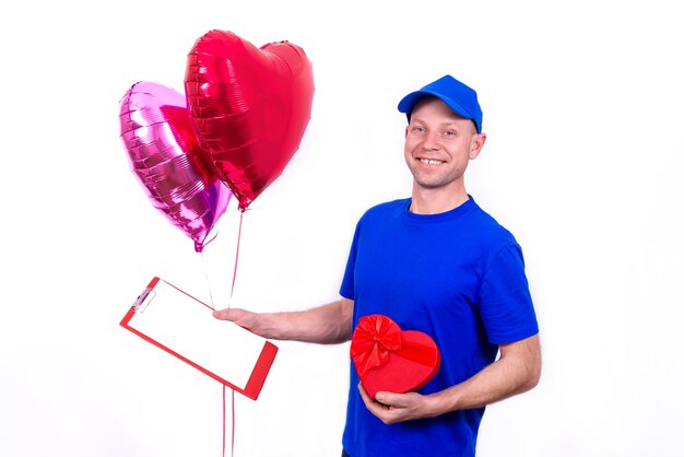 Courier in blue uniform holds red heart-shaped gift box and balloon for Valentine's Day