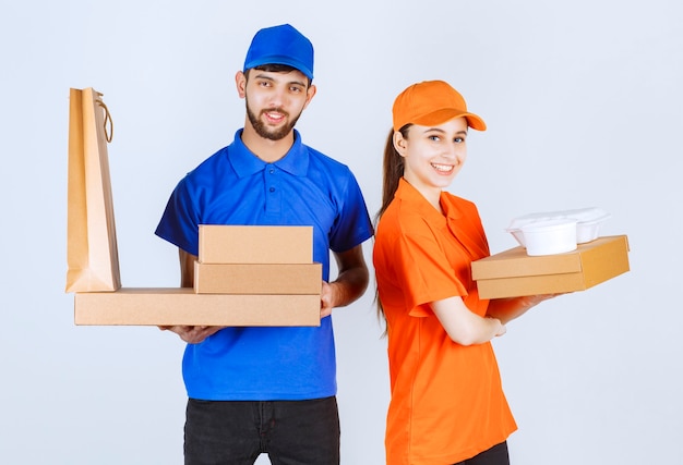 Courier boy and girl in blue and yellow uniforms holding cardboard takeaway boxes and shopping packages.