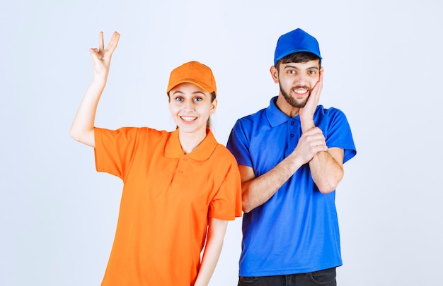 Foto ragazzo e ragazza del corriere in uniformi blu e gialle che mostrano il segno di gioia e di felicità.