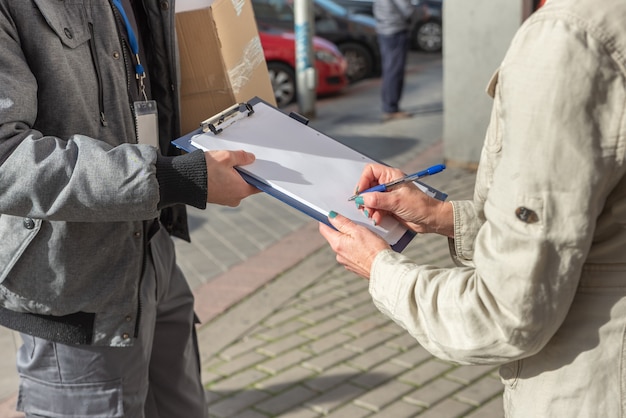 Courier delivering order to woman who signs for delivery of package, up close