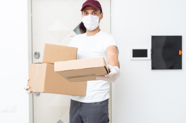 Courier, delivery man in medical latex gloves and mask safely delivers online purchases in white box to the door during the coronavirus epidemic, COVID-19. Stay home, safe concept.