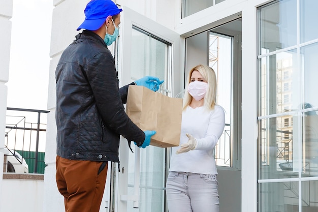 Courier, delivery man in protective mask and medical gloves delivers takeaway food. Delivery service under quarantine, disease outbreak, coronavirus covid-19 pandemic conditions. Stay home