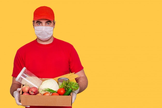 Un impiegato di corriere in uniforme detiene una scatola di cartone con cibo, indossando maschera, concetto di coronavirus