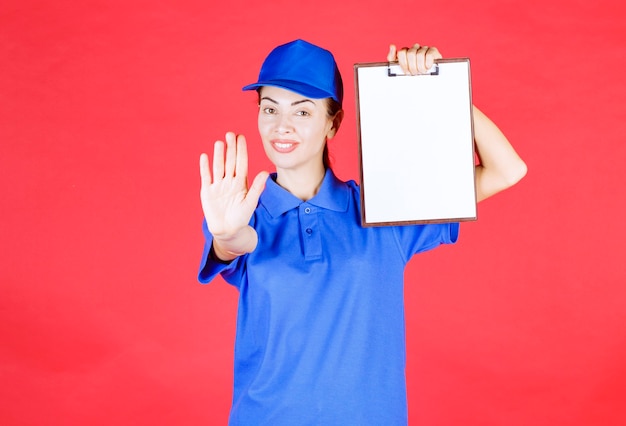 Photo courier girl in blue uniform holding a tasklist and stopping someone.