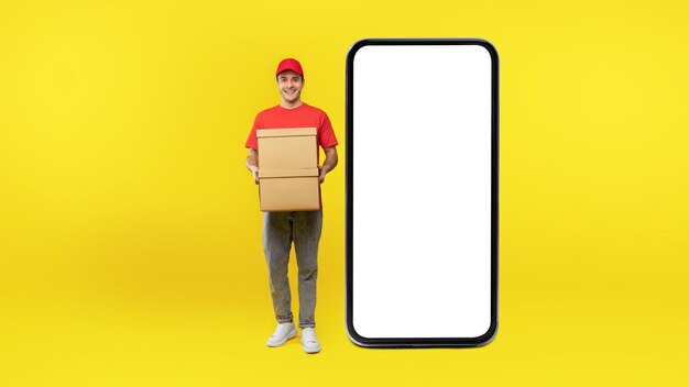 Courier Guy Posing Near Huge Cellphone Holding Boxes Yellow Background