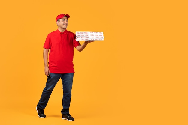 Courier guy in uniform presents takeaway pizza boxes yellow backdrop