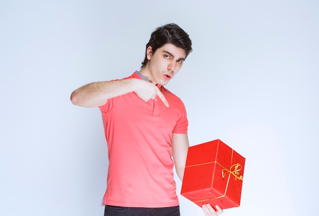 Курьер держит красные подарочные коробки и указывая на него.