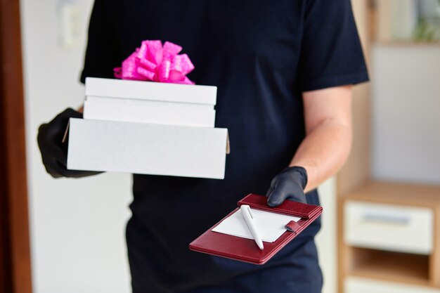 Courier man in black with protection medical mask and gloves contactless delivery presents, gift box during a coronavirus epidemic