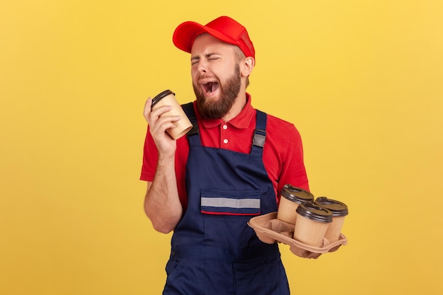 Il corriere tiene in mano tazze di caffè e piange sentendosi esausto e annoiato dopo che il lavoro stressante ha bisogno di energia