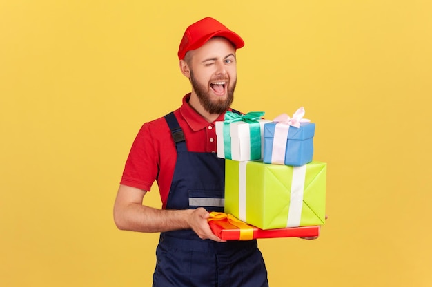 Courier man holding many present boxes bringing order for celebrating holiday winking to camera