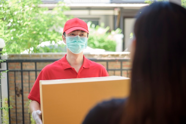 Человек-курьер в защитной маске и перчатках доставляет коробку с едой во время вспышки вируса. Безопасная доставка на дом.