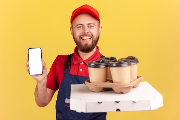 Courier man with pizza box and coffee in disposable cup and showing cell phone with blank screen