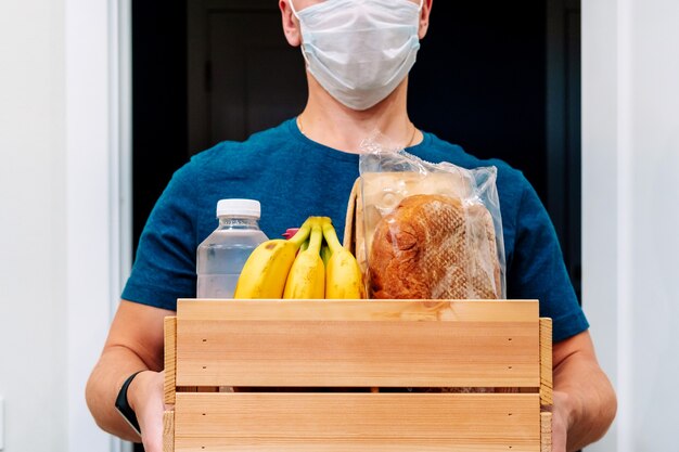 A courier in a mask delivers a box of food items. Service delivery in terms of quarantine