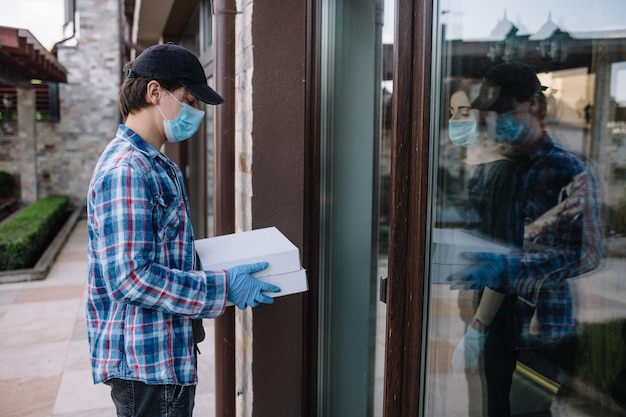 Courier in protective mask delivers parcel customer in medical gloves receives box Delivery service under quarantine disease outbreak coronavirus covid19 pandemic conditions