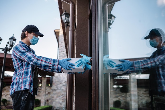 Courier and protective mask delivers parcels customer and medical gloves receives box Delivery service under quarantine disease outbreak coronavirus covid19 pandemic conditions