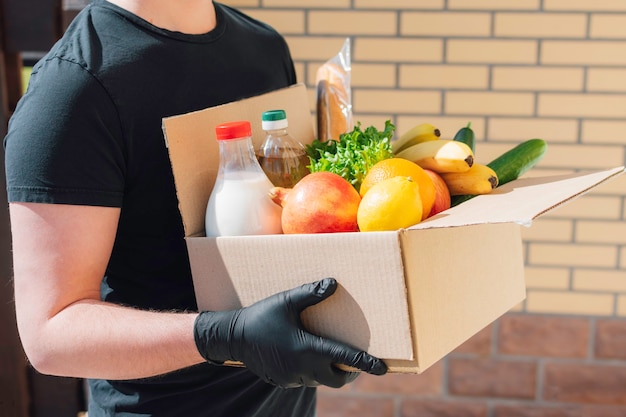 Foto il corriere in maschera protettiva e guanti consegna una scatola di cibo diverso