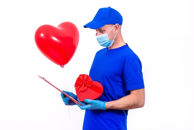 Courier in protective mask, gloves holds red heart-shaped gift box and balloon for Valentine's Day