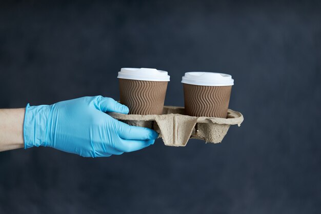 Courier in protective mask and medical gloves delivers takeaway food and coffee. Delivery service under quarantine, disease outbreak, coronavirus covid-19 pandemic conditions.