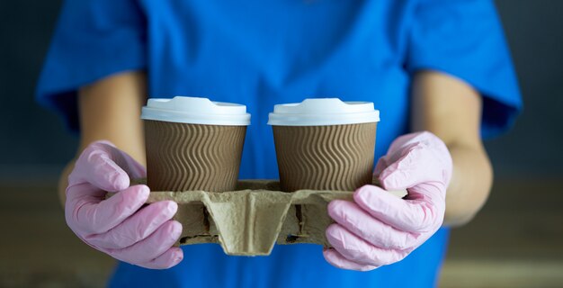 Photo courier in protective mask and medical gloves delivers takeaway food and coffee. delivery service under quarantine, disease outbreak, coronavirus covid-19 pandemic conditions.