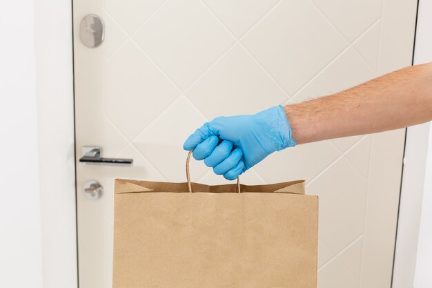 Courier in protective mask and medical gloves delivers takeaway food. Delivery service under quarantine, disease outbreak, coronavirus covid-19 pandemic conditions.