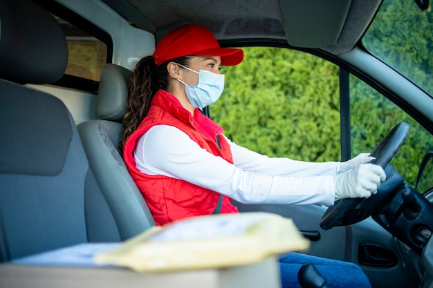 courier with mask driving van and delivering parcels during corona virus or covid19 pandemic