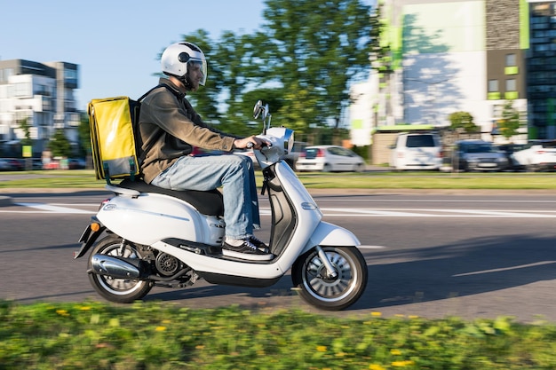 A courier with a yellow bag on a scooter is going to give an order to a customer Photography in motion selective focus on a man