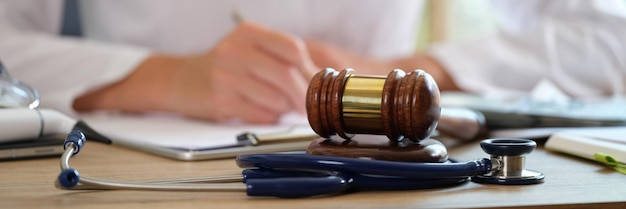 Photo court gavel with stethoscope on a table in background doctor writes notes concept of medical