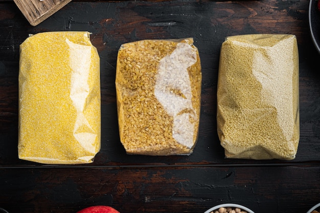 Couscous, bulgur and polenta in pounch, top view on dark wooden table.