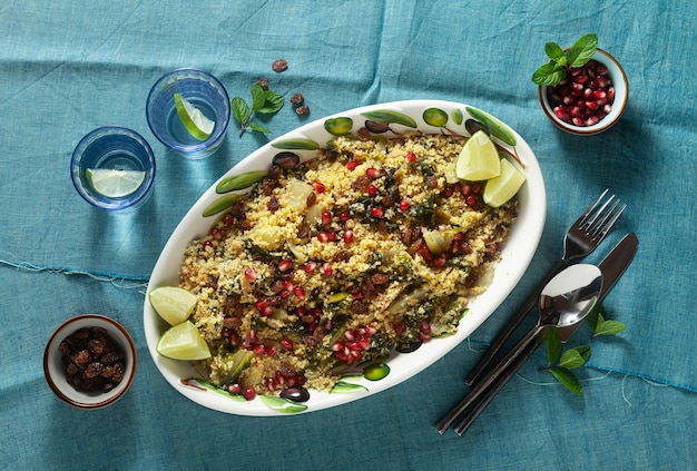 Couscous is cooked on orange juice with boiled vegetables, caramelized onions, raisins and pomegranate seeds. on the table with a linen tablecloth