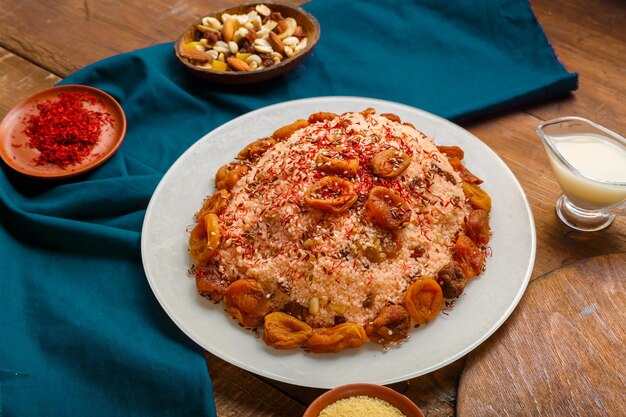 Couscous masfouf with dried fruits in a plate on a wooden table next to saffron and couscous