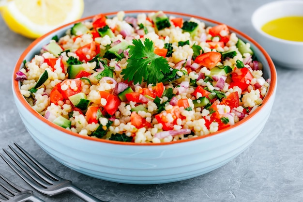 Insalata di couscous tabbouleh con pomodori freschi, cetrioli e cipolle rosse in una ciotola su sfondo di pietra grigia