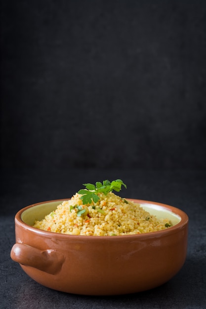 Couscous with vegetables in bowl on black stone copy space