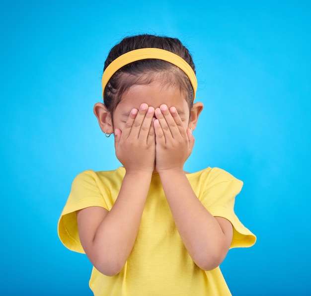 Cover eyes hands on face and child on blue background for shy mistake expression and sad in studio emotion reaction childhood and young girl isolated for hide and seek surprise and blind emoji