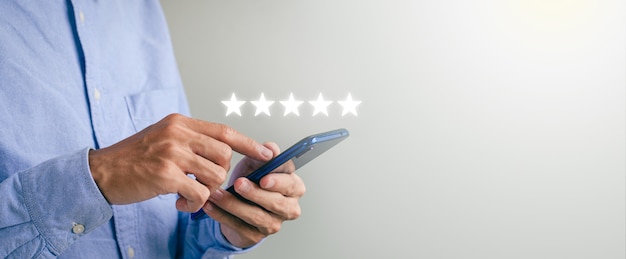 Cover the guy's hand using a smartphone and give the five-star symbol to increase the customer service rating of the company concept. customer service experience and satisfaction surveys