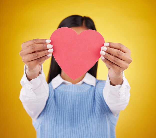 Cover paper and heart with woman in studio for love support and romance valentines day kindness and date with female hiding with symbol on yellow background for health happiness and hope mockup