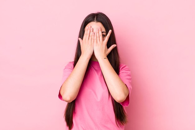 Covering face with hands peeking between fingers with surprised expression and looking to the side