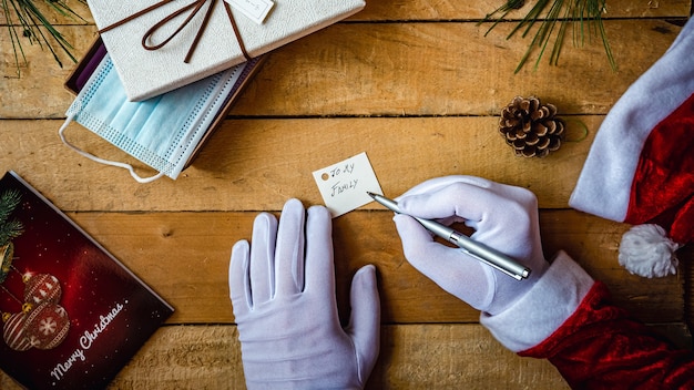 Covid-19 Christmas shot of Santa Claus hands in white gloves writing "To my family" on a card