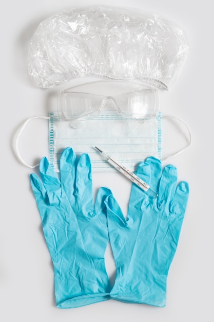 Covid-19-concept. Een set beschermende kleding en een thermometer. Hoed, bril, handschoenen, schoenovertrekken en een masker. Preventie en temperatuurmeting