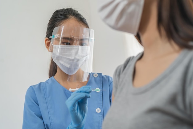 Covid-19, coronavirus asian young woman getting vaccine from doctor or nurse giving syringe shot to arm's patient. Vaccination, immunization, disease prevention against flu or virus pandemic concept.