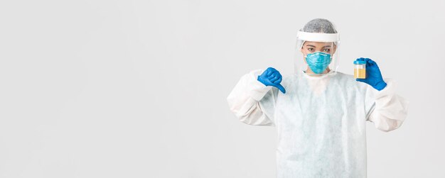 Covid-19, coronavirus disease, healthcare workers concept. Side view of serious tech lab employee, researcher in personal protective equipment show thumb-down in disapproval, bad analyze result