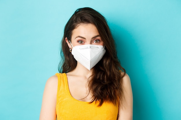 Covid-19, coronavirus and social distancing. Attractive young woman wearing respirator from coronavirus, looking at camera, blue background