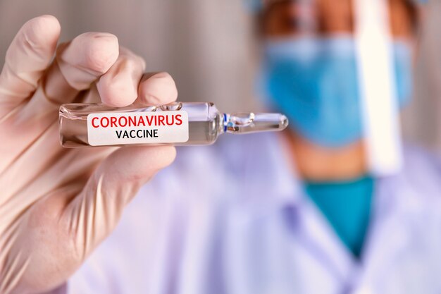 Covid-19, vaccino contro il coronavirus. chiudere le mani dello scienziato mostrano il vaccino covid-19 in una fiala di vetro. le mani del medico indossano un guanto di lattice bianco che tiene il vaccino covid-19 in una fiala di vetro.