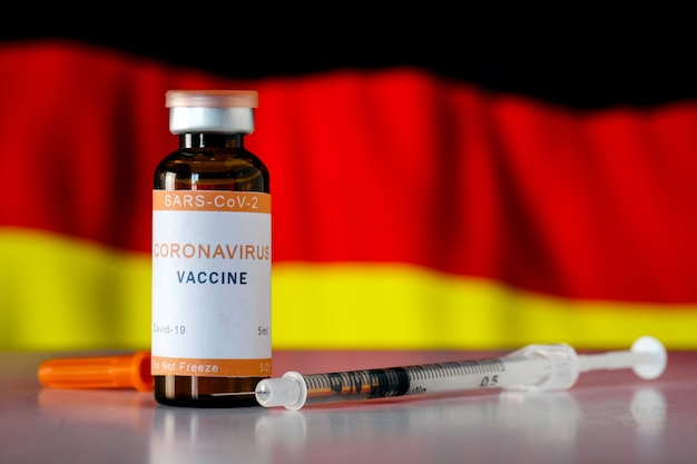 Covid 19 coronavirus vaccine with a dose in a syringe against the background of the German flag. The concept of vaccination and immunization against coronavirus in Germany.