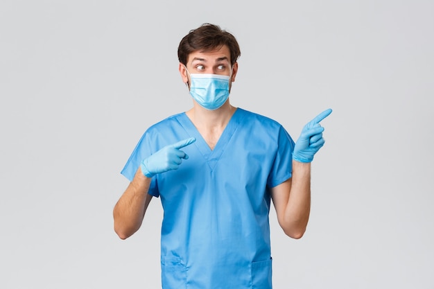 Covid-19, gezondheidswerkers en ziekenhuisconcept. opgewonden mannelijke arts in scrubs, medisch masker en handschoenen, wijzende vingers naar rechts, coronavirusinfo tonend, informatie over behandeling