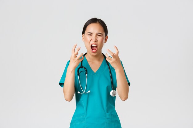 Covid-19, healthcare workers and preventing virus concept. Angry pissed-off asian female nurse, doctor losing temper, stressed-out physician shouting in anger, looking mad and aggressive.