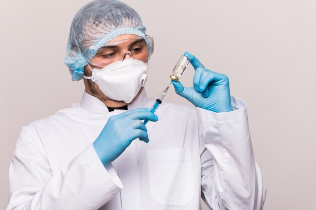 COVID-19 infection. Male doctor examines medicine for illness, man in blue mask with syringe and jar