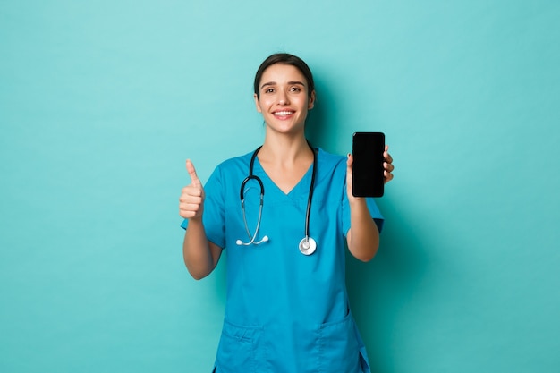 Covid-19, pandemic and medicine concept. Image of smiling beautiful female doctor, wearing scrubs