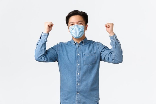 Covid-19, preventing virus, and social distancing at workplace concept. Successful winning asian businessman encourage good team spirit, raising hands up in rejoice, wearing medical mask