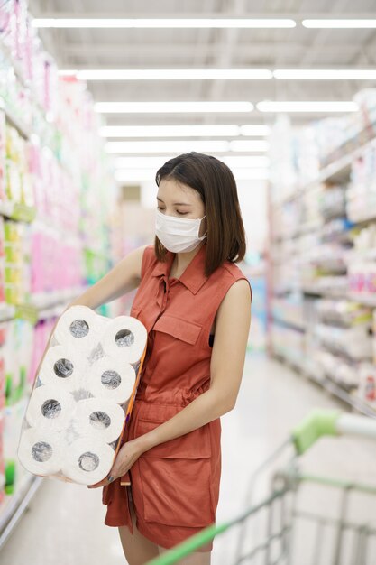 Covid-19 spreading outbreak. Woman in medical protective mask panic buying tissue paper. Fear of coronavirus.